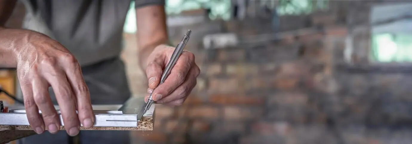 A carpenter holds a ruler and a pencil while marking the wood.