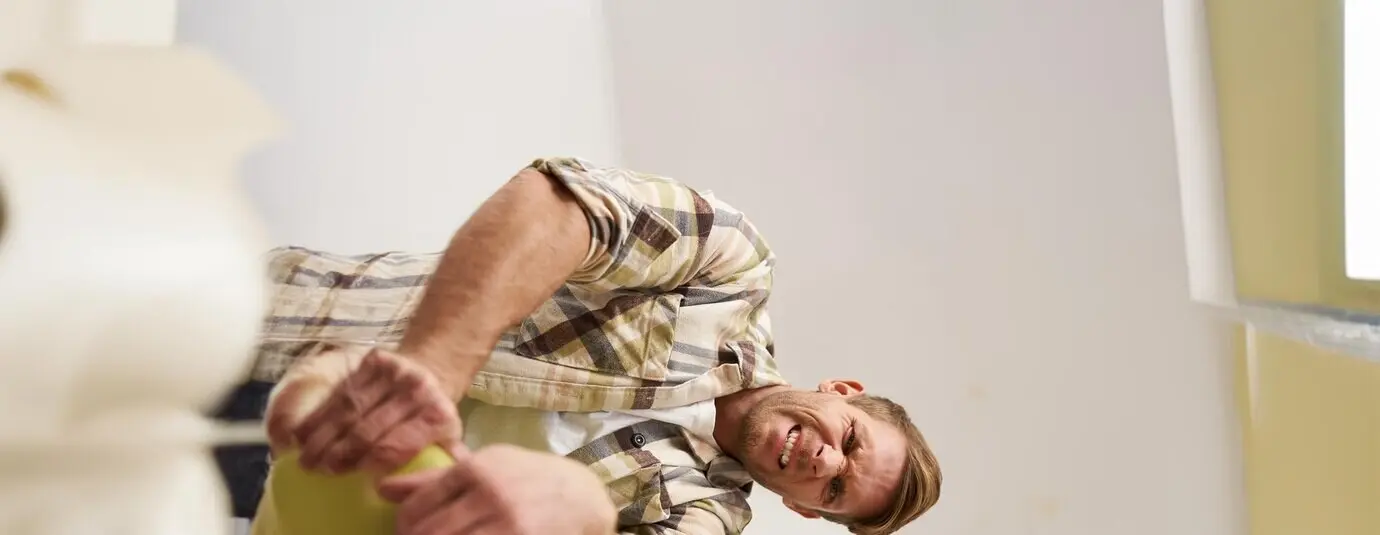Image of a funny man trying to close a suitcase filled with a pile of clothes while packing luggage and putting things inside the bag.